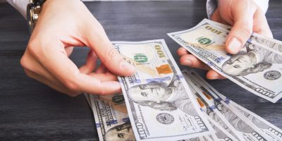 Hands with watch counting dollar bank notes on dark wooden table