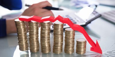 Close-up Of Red Arrow Over Decreasing Stacked Coins Showing Downward Direction