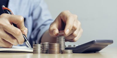 Businessmen are using pens to Record the amount of Money coins for Plans to Accountancy on wood table stack in office at home, with copy space.Accounting and financial economic calculation concepts.