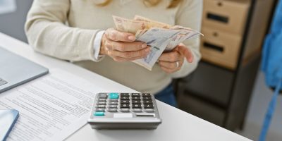 Hispanic woman holding colombian pesos in a modern office setting.