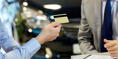 auto business, sale and people concept - close up of customer giving credit card to car dealer in auto show or salon